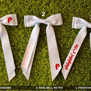 May include: Three light blue hair bows with red and white text. The first bow has the text "dancing on my own". The second bow has the text "THE RING BELL". The third bow has the text "Phightin' Phils".