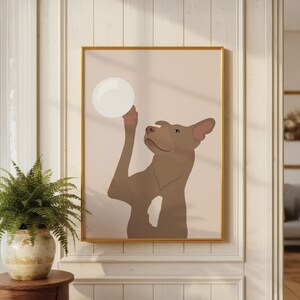 May include: A framed art print showing a brown dog with a white bubble. The dog is illustrated in a minimalist style against a light pink backdrop. The frame is gold, and the artwork is displayed on a white wall.