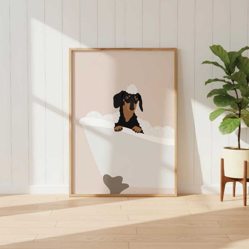 May include: A framed print showing a black and brown dachshund dog in a bathtub with bubbles. The dog wears a white bubble bath hat. The background is a light pink colour.