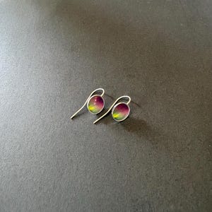 May include: A pair of silver drop earrings featuring small, oval-shaped charms. Each charm displays a vibrant gradient pattern that transitions from deep purple at the top to a bright lime green at the bottom, set within a thin silver frame.