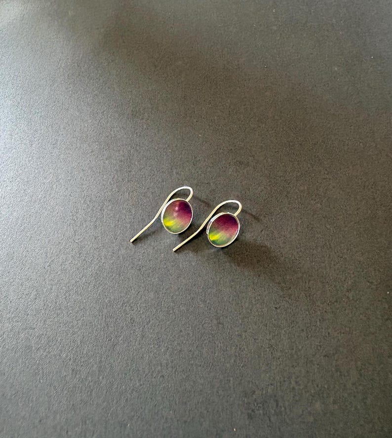 May include: A pair of silver drop earrings featuring small, oval-shaped charms. Each charm displays a vibrant gradient pattern that transitions from deep purple at the top to a bright lime green at the bottom, set within a thin silver frame.