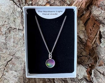 May include: A silver chain necklace with a circular pendant featuring a colorful, iridescent gradient of green, purple, and pink hues. The jewelry is presented in a white box with a black insert labeled The Northern Light Hand made.