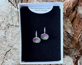 May include: A pair of oval-shaped earrings with silver-toned metal settings and iridescent, multi-colored surfaces featuring green and purple hues. The earrings are displayed in a white box with a black insert labeled The Northern Light Hand made.