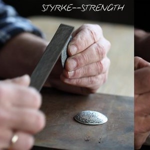 May include: A three-part sequence showing metalworking steps. The first panel shows a metal stamp on a disc with the text N&Oslash;YAKTIGHET--ACCURACY. The second shows filing a disc with STYRKE--STRENGTH. The third shows painting a disc with T&Aring;LMODIGHET--PATIENCE.