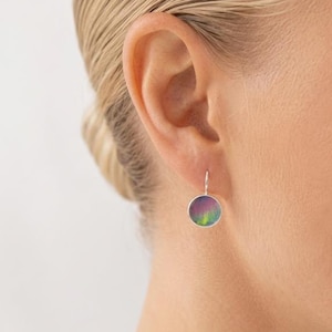 May include: A circular drop earring featuring a metallic silver frame and a vibrant, multi-colored inlay with swirling hues of purple, pink, and green. The earring hangs from a simple silver hook, displaying a smooth, polished surface finish.