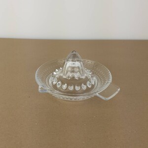 May include: A clear glass citrus juicer with a pointed top and a wide base. The base has a textured design and a handle on each side.