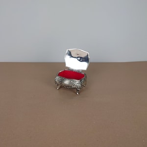 May include: A silver trinket box with an ornate design and a red velvet interior. The box is open and the lid is propped up.