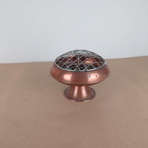 Peut inclure: Un vase à fleurs en cuivre avec un dessus en grillage métallique. Le vase a une base ronde et un dessus en forme de bol.
