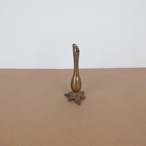 May include: A small, vintage brass bud vase. The vase has a slender, elongated body with a flared top. The base is a starburst design with leaf and grape details. The vase is approximately 15 cm tall.