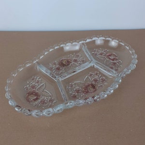 Puede incluir: Un plato de servir de vidrio transparente con tres secciones divididas. El plato tiene un borde festoneado y un diseño floral con rosas rosas.