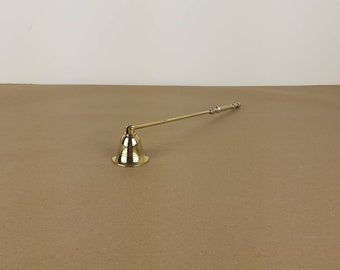 May include: A gold candle snuffer with a long handle. The snuffer is shaped like a bell and has a decorative design on the handle.