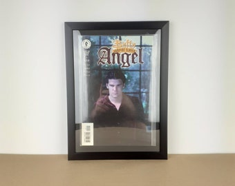 May include: A black framed comic book featuring a character named Angel from the Buffy the Vampire Slayer series. The cover features a close-up of Angel's face with a dark background and a window behind him.