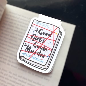 May include: A white sticker with a red and black illustration of a book titled "A Good Girl's Guide to Murder" by Holly Jackson. The book cover is covered in red string and has several push pins.