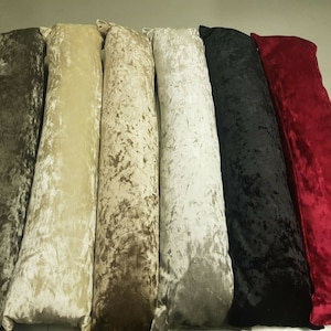 May include: Six long, rectangular cushions in various colours, including brown, beige, grey, black, and red. The cushions are made of a soft, velvety fabric with a crushed velvet texture.