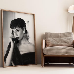 Peut inclure: Photographie en noir et blanc d'une femme en robe noire parlant au t&eacute;l&eacute;phone. La photo est encadr&eacute;e dans un cadre en bois et est accroch&eacute;e au mur.