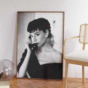Peut inclure: Photographie en noir et blanc d'une femme aux cheveux courts, portant une robe noire et tenant un t&eacute;l&eacute;phone rotatif vintage &agrave; son oreille. La photo est encadr&eacute;e dans un cadre en bois brun.