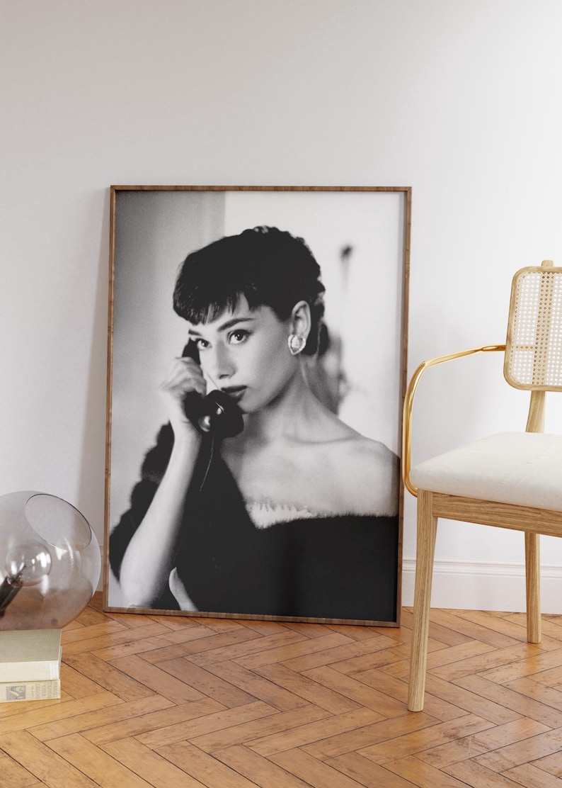 Peut inclure: Photographie en noir et blanc d'une femme aux cheveux courts, portant une robe noire et tenant un t&eacute;l&eacute;phone rotatif vintage &agrave; son oreille. La photo est encadr&eacute;e dans un cadre en bois brun.