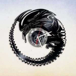 May include: A black vinyl record clock featuring a silhouette of the Alien creature from the movie franchise. The clock face is a circular design with Roman numerals and gears.