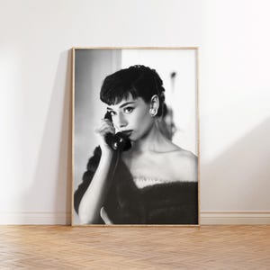 Peut inclure: Photographie en noir et blanc d'une femme aux cheveux courts et fonc&eacute;s, portant un col en fourrure et tenant un t&eacute;l&eacute;phone rotatif vintage &agrave; son oreille.