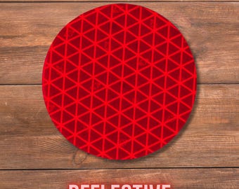 May include: A circular red reflective decal featuring a repeating geometric pattern of interconnected triangles. The surface has a distinct grid-like texture designed for high visibility, and the word REFLECTIVE is printed in bold white capital letters.