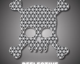 May include: A reflective skull and crossbones design with a geometric pattern of white triangles on a dark grey background. The word "REFLECTIVE" is displayed in white block letters below the skull.