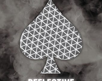 May include: A spade-shaped decal featuring a white geometric triangular grid pattern on a dark grey background. The word REFLECTIVE is printed in white capital letters at the bottom of the image, set against a swirling grey smoke effect.