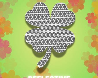 May include: A four-leaf clover shape featuring a dark gray surface with a repeating white triangular grid pattern. The clover is centered against a bright lime green background decorated with a border of orange and pink flower silhouettes.