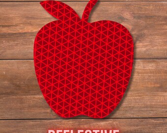 May include: A red reflective apple-shaped sticker with a geometric pattern, set against a wooden background. The word "REFLECTIVE" is displayed in a red font at the bottom of the image.