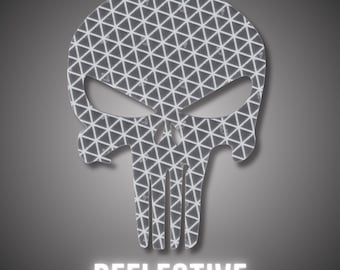 May include: A reflective skull-shaped sticker with a geometric pattern. The design is grey and white, with the word "REFLECTIVE" in white block letters at the bottom. The sticker is likely for vehicles or safety applications.