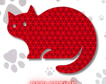 May include: A red cat-shaped sticker featuring a repeating triangular geometric pattern across its surface. The sticker has two circular cutouts for eyes and the word REFLECTIVE printed in red capital letters at the bottom of the design.