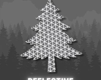 May include: A silver-toned, reflective Christmas tree cutout featuring a repeating geometric triangle pattern across its surface. The word REFLECTIVE is printed in bold, white, sans-serif capital letters directly below the tree shape.