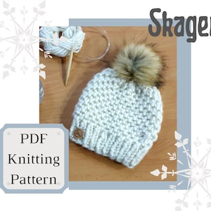 Op de afbeelding: Een witte gebreide beanie met een bruine nep bont pompon. De beanie ligt op een houten oppervlak met een bol wol en breinaalden. De tekst "PDF Knitting Pattern" staat in een blauwe doos aan de linkerkant van de afbeelding. De tekst "Skagen" staat in een blauwe doos aan de rechterkant van de afbeelding.