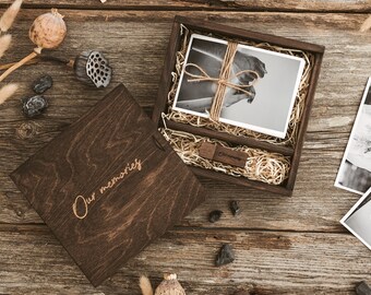 May include: A wooden box with a lid that says "Our memories" on the top. The box is filled with brown paper and a black and white photo. A USB drive is also included in the box.