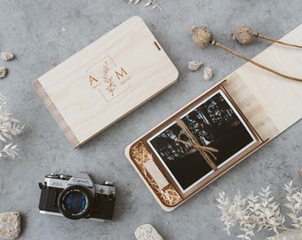 May include: Two wooden boxes, one closed and one open, with photos inside. The closed box has the initials "A M" and the word "married" engraved on it. A vintage camera and decorative elements are also present.