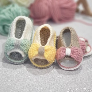 Pode incluir: Tr&ecirc;s pares de sand&aacute;lias de beb&eacute; de croch&ecirc; com la&ccedil;os de diferentes cores. As sand&aacute;lias s&atilde;o em tons de cinza, amarelo e rosa.