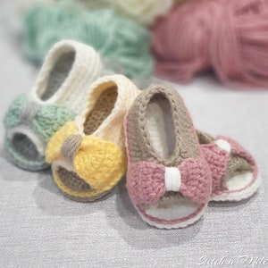 Pode incluir: Tr&ecirc;s pares de sand&aacute;lias de beb&eacute; de croch&ecirc; com la&ccedil;os de diferentes cores. As sand&aacute;lias s&atilde;o bege, branco e castanho com la&ccedil;os amarelos, cor-de-rosa e verdes.