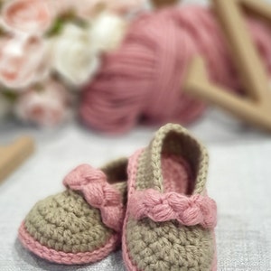Pu&ograve; includere: Un paio di scarpine per neonati all'uncinetto in beige con bordi e fiocchi rosa. Le scarpine sono realizzate con un punto a trama e hanno un aspetto morbido e confortevole.