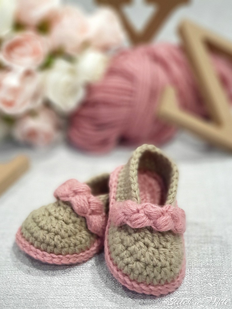 Pu&ograve; includere: Un paio di scarpine per neonati all'uncinetto in beige con bordi e fiocchi rosa. Le scarpine sono realizzate con un punto a trama e hanno un aspetto morbido e confortevole.