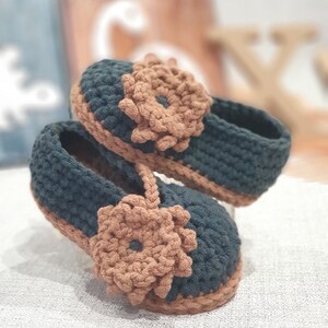 Pu&ograve; includere: Un paio di scarpine per neonati all'uncinetto in verde scuro e marrone con un dettaglio floreale su ogni scarpa.