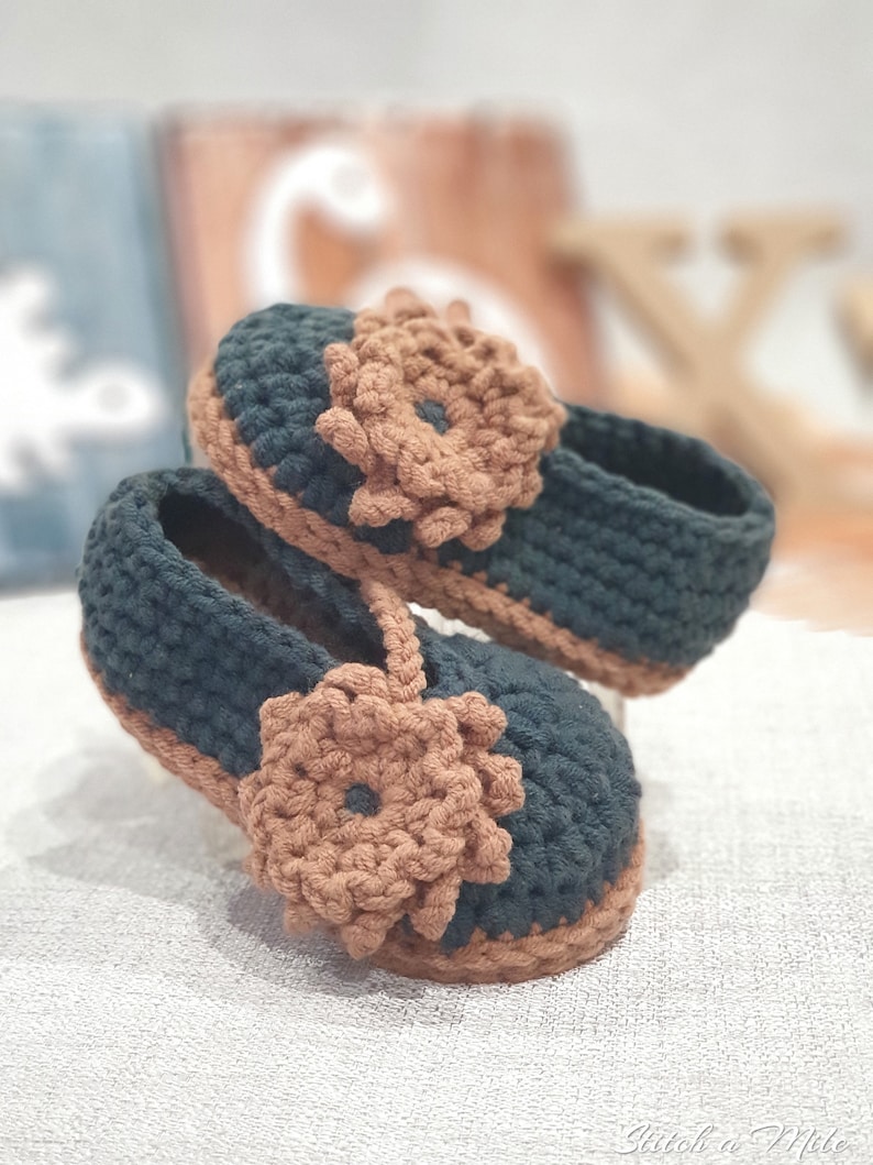 Pu&ograve; includere: Un paio di scarpine per neonati all'uncinetto in verde scuro e marrone con un dettaglio floreale su ogni scarpa.