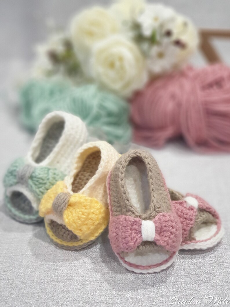 Pode incluir: Tr&ecirc;s pares de sand&aacute;lias de beb&eacute; de croch&ecirc; com la&ccedil;os de diferentes cores. As sand&aacute;lias s&atilde;o bege, branco e castanho com la&ccedil;os amarelos, cor-de-rosa e verdes.