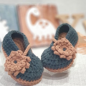 Pu&ograve; includere: Un paio di scarpine per neonati all'uncinetto in verde scuro e marrone con un dettaglio floreale su ogni scarpetta.