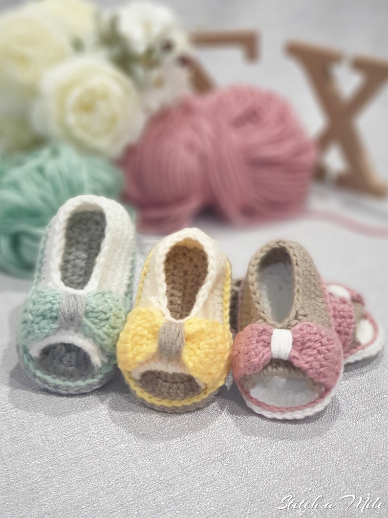 Pode incluir: Tr&ecirc;s pares de sand&aacute;lias de beb&eacute; de croch&ecirc; com la&ccedil;os de diferentes cores. As sand&aacute;lias s&atilde;o em tons de cinza, amarelo e rosa.