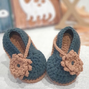 Pu&ograve; includere: Un paio di scarpine per neonati in crochet verde scuro con dettagli floreali marroni. Le scarpine hanno un cinturino che passa intorno alla caviglia.