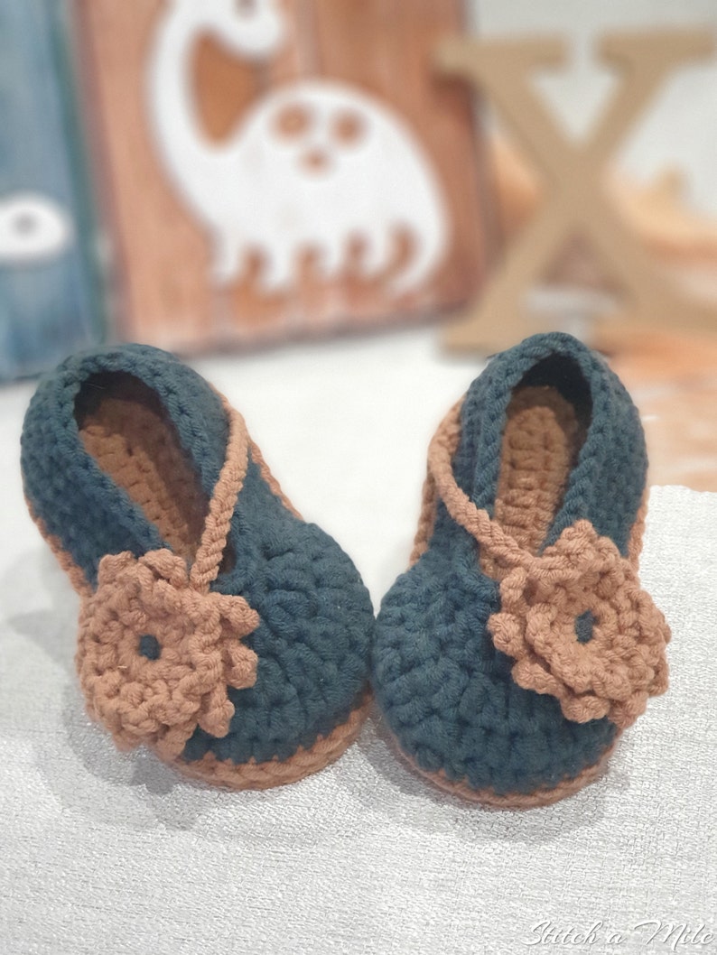 Pu&ograve; includere: Un paio di scarpine per neonati in crochet verde scuro con dettagli floreali marroni. Le scarpine hanno un cinturino che passa intorno alla caviglia.