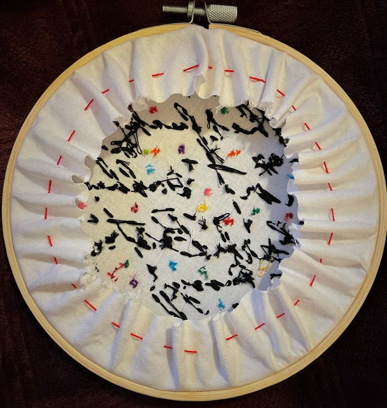 May include: A white embroidery hoop with a black and white design embroidered on white fabric. The design features black lines and colorful dots. The hoop is made of wood and has a diameter of approximately 8 inches.