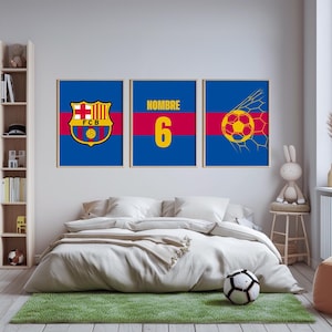 Puede incluir: Tres impresiones enmarcadas con temática de fútbol. Las impresiones presentan el logotipo del FCB, la palabra "NOMBRE" encima del número 6 y un balón de fútbol en una red. Las impresiones tienen un fondo azul con detalles en rojo y amarillo. Un balón de fútbol está sobre una alfombra verde.