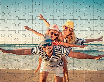 Puede incluir: Una familia de tres en una playa, el padre lleva a su hija y a su hijo en la espalda, los tres llevan sombreros y gafas de sol, el padre lleva una camisa a rayas, la madre lleva una camisa a rayas, la hija lleva una camisa a rayas rojas y blancas, el hijo lleva una camisa a rayas azules y blancas, la playa es arenosa y el agua es azul.