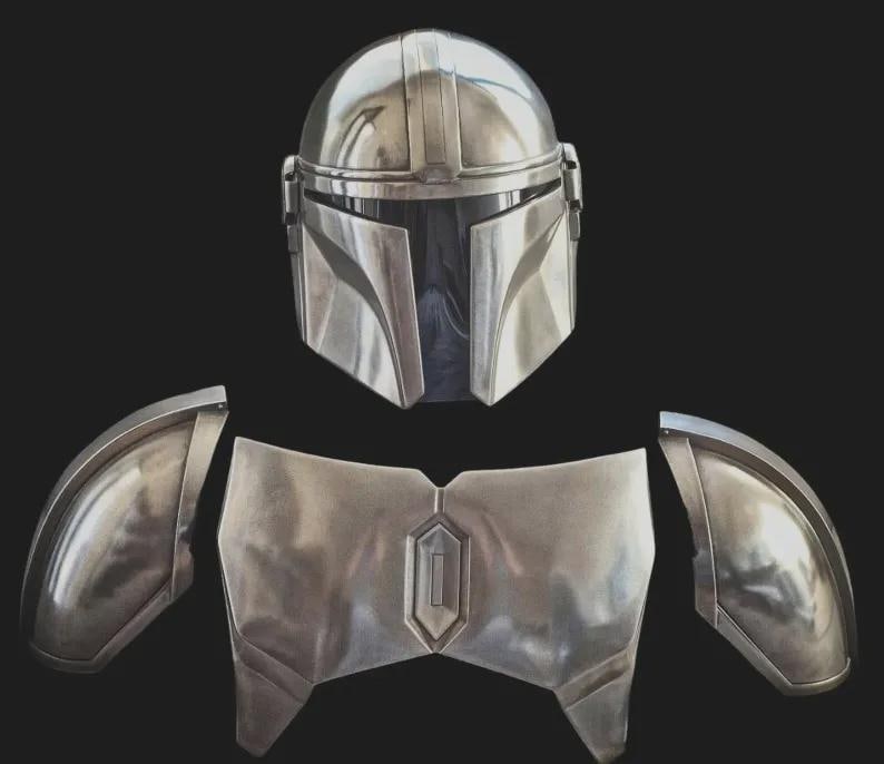May include: A metallic silver helmet with a T-shaped visor and a matching chest plate with two separate shoulder pauldrons. The armour pieces feature a smooth, reflective finish and geometric contours, presented as a set of costume components.