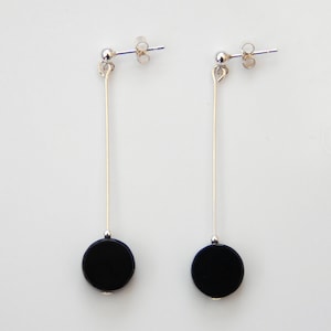 May include: A pair of silver dangle earrings with black round stones at the bottom.